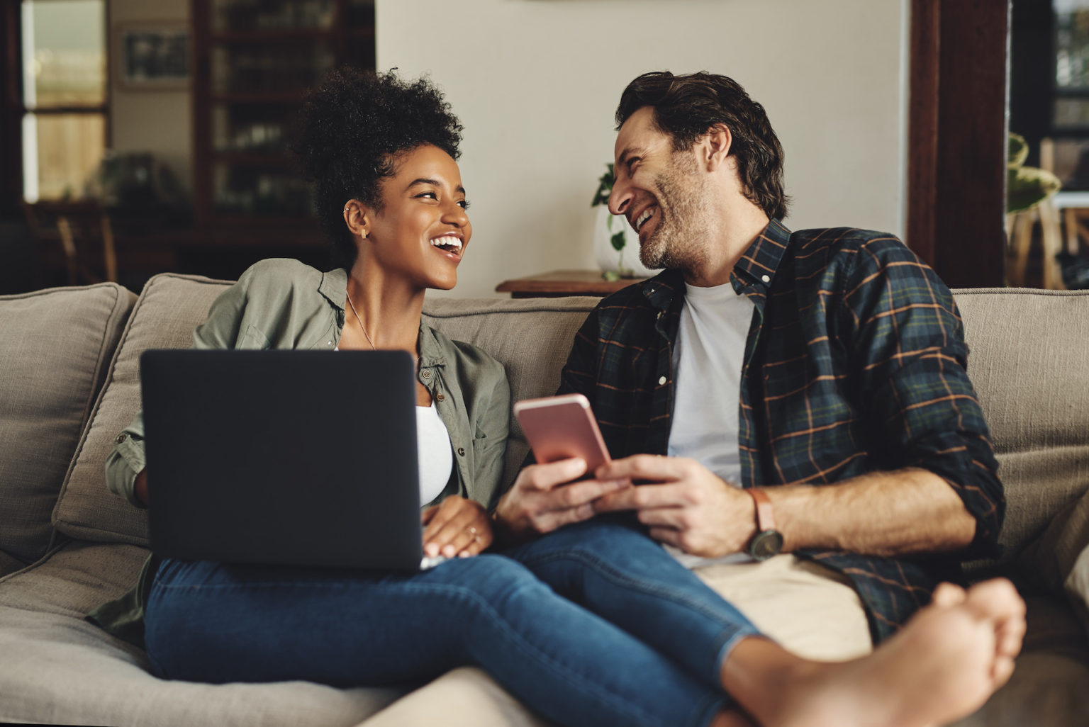 Shot of a happy young couple using a laptop and cellphone while relaxing on a couch home