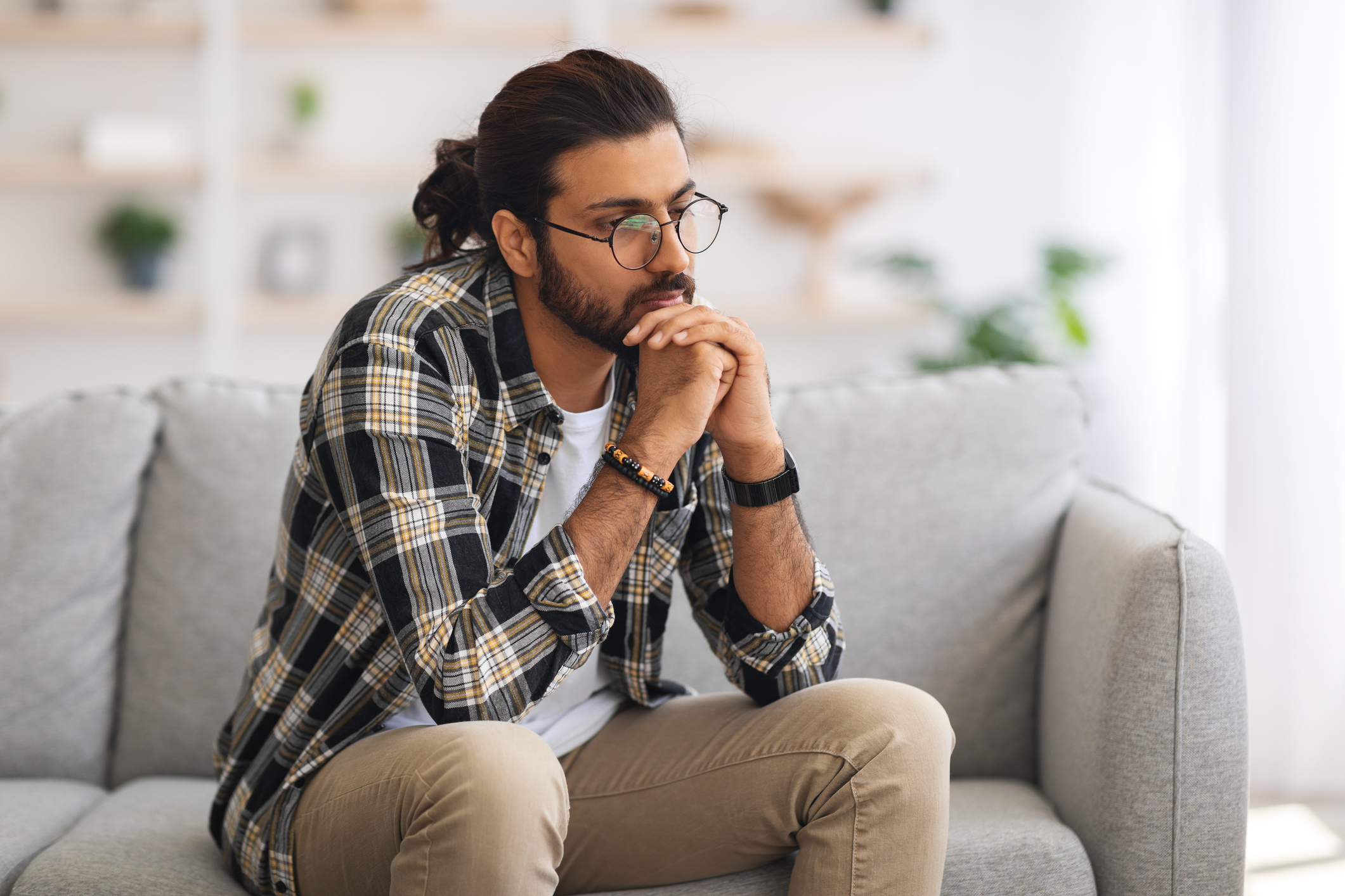 A man sits on a couch and rests his chin on hands as he reflects and practices self-care