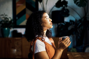 Young Black Woman closes her eyes peacefully as she holds a cup of coffee
