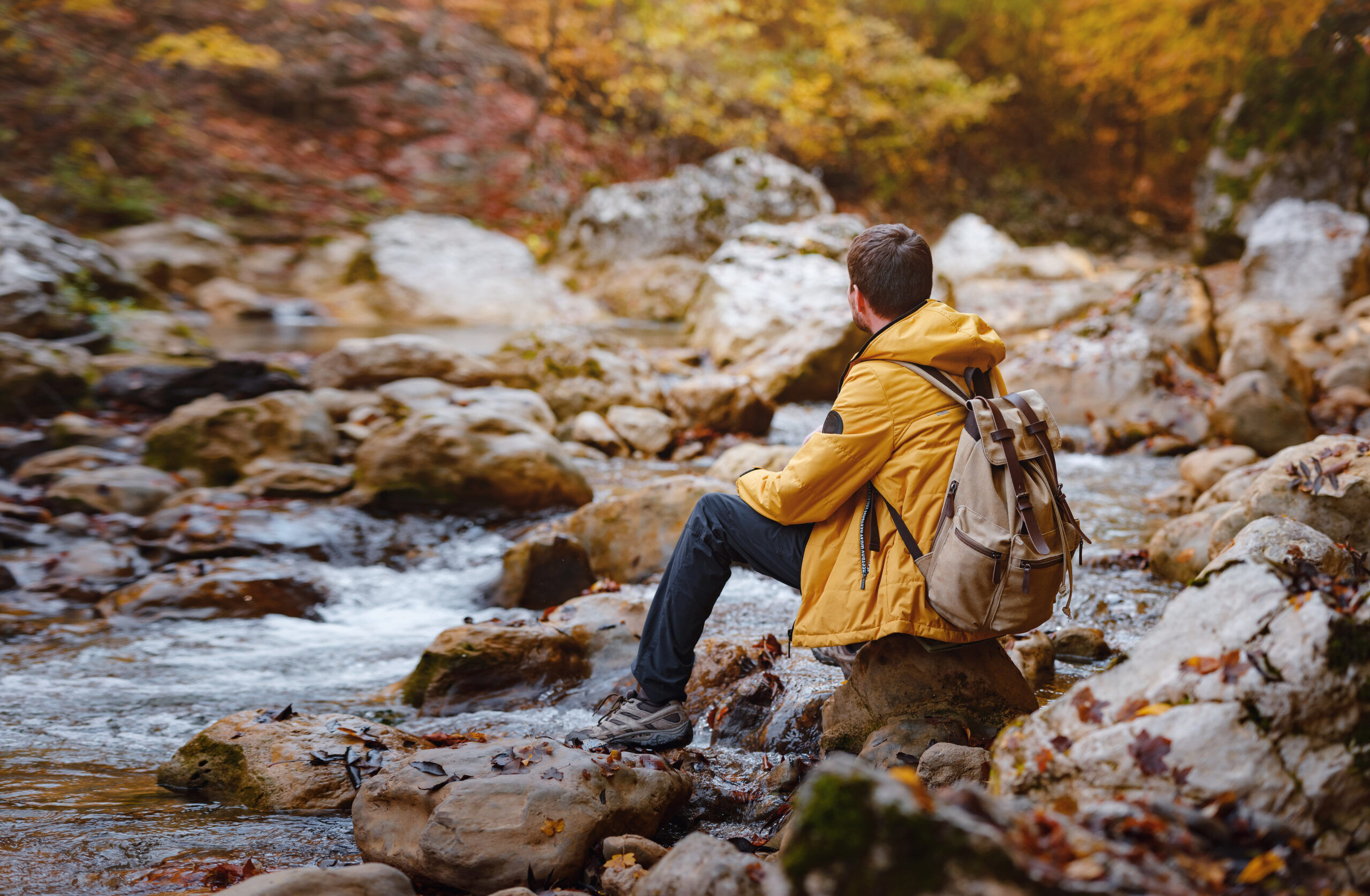 Man in hiking clothes sits on rocky riverbank reflecting