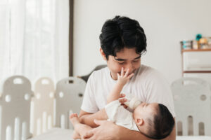 Father holds and feeds baby from bottle while smiling at the baby